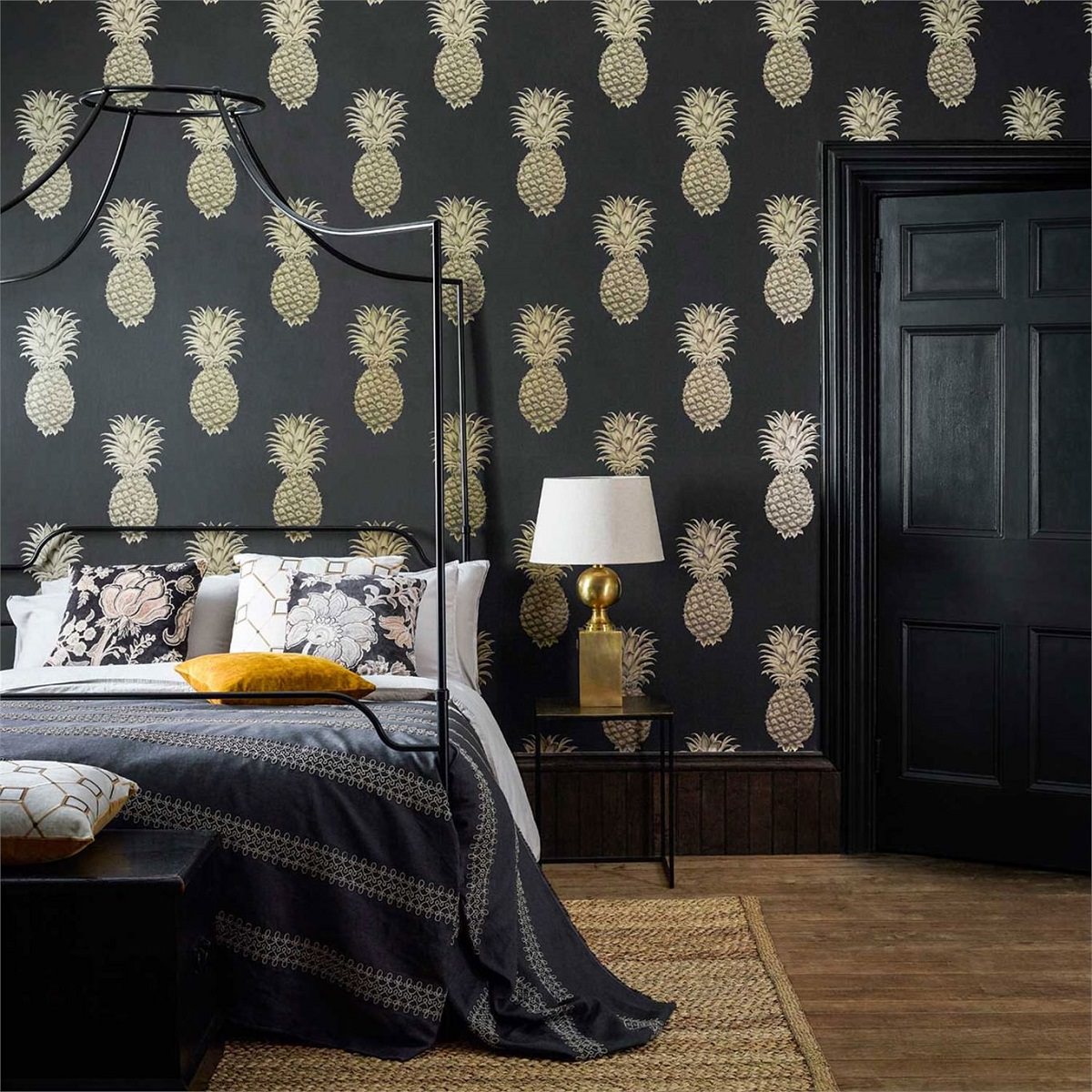 دکوراسیون داخلی اتاق خواب با کاغذ دیواری مشکی و تخت فلزی سایبان دار که از الگوهای آناناس روی دیوار آن استفاده شده است